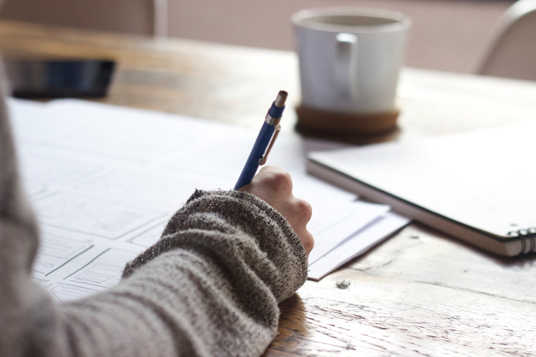 A hand writing on a wooden table near a mug, grading at the kitchen table
