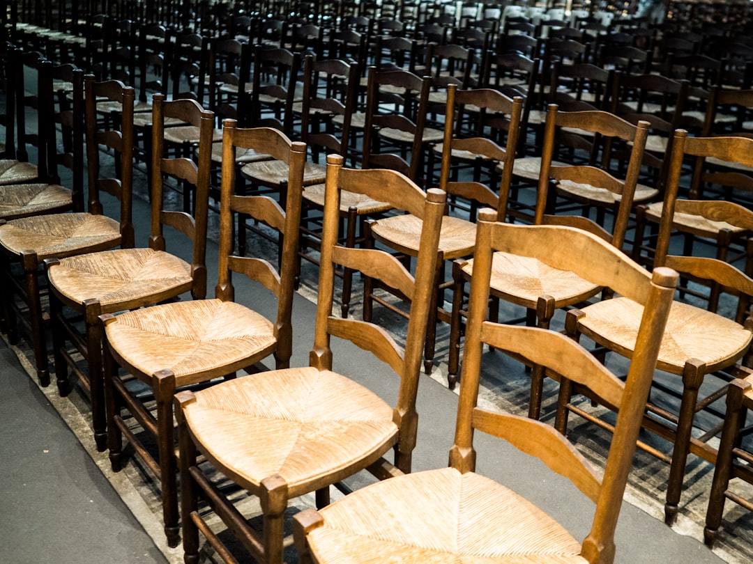 Rows of empty wooden chairs with woven seats in a meeting hall, the room before six families arrive
