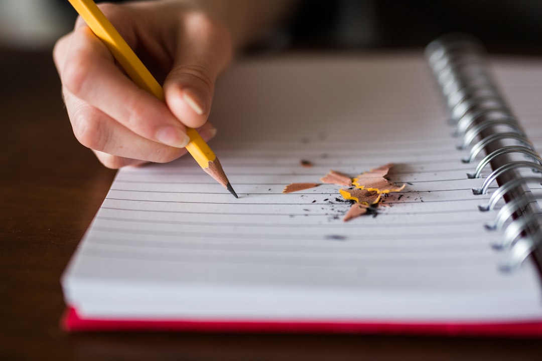 A hand holding a pencil, writing in a notebook, working through the day's lesson at the table