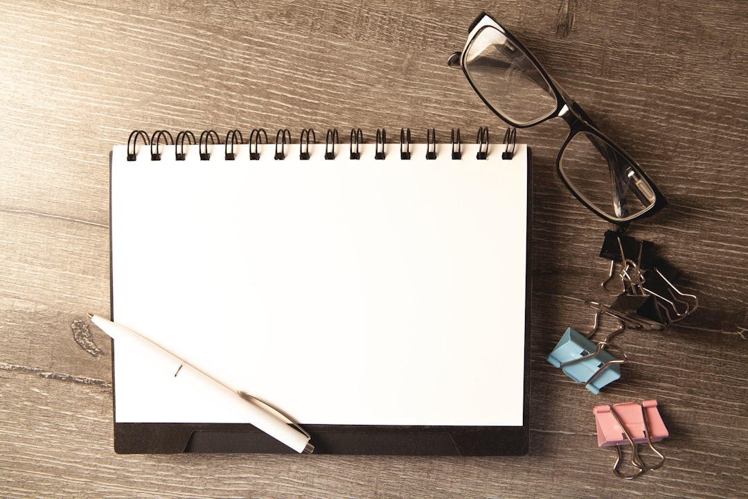 A notepad, pen, and reading glasses laid out on a wooden desk, the application filled out before it becomes a record