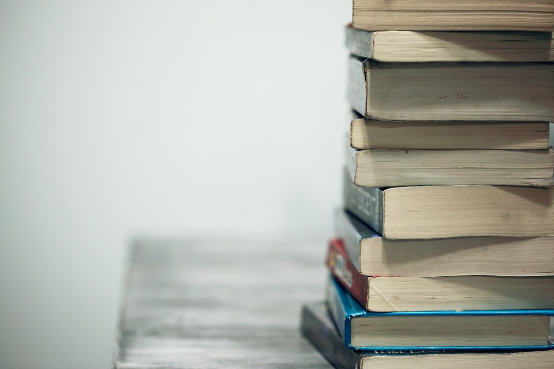 A stack of assorted textbooks on a wooden table, set out for a home-day course load